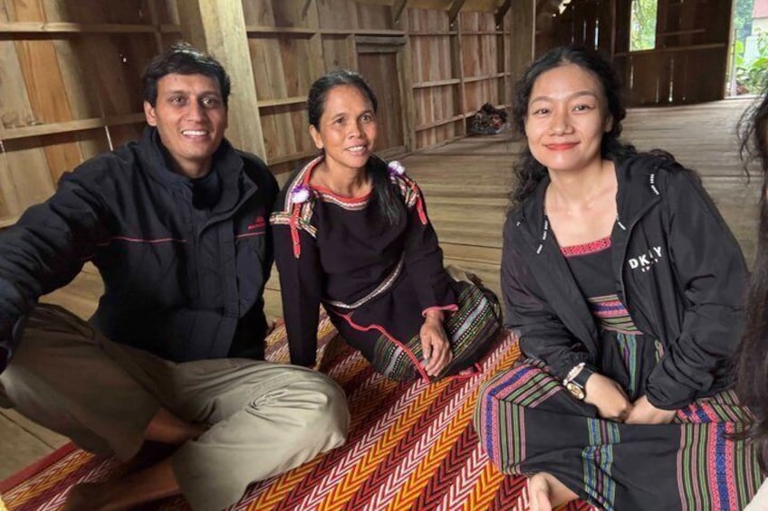 Three people sitting on a patterned mat in a wooden structure. 3