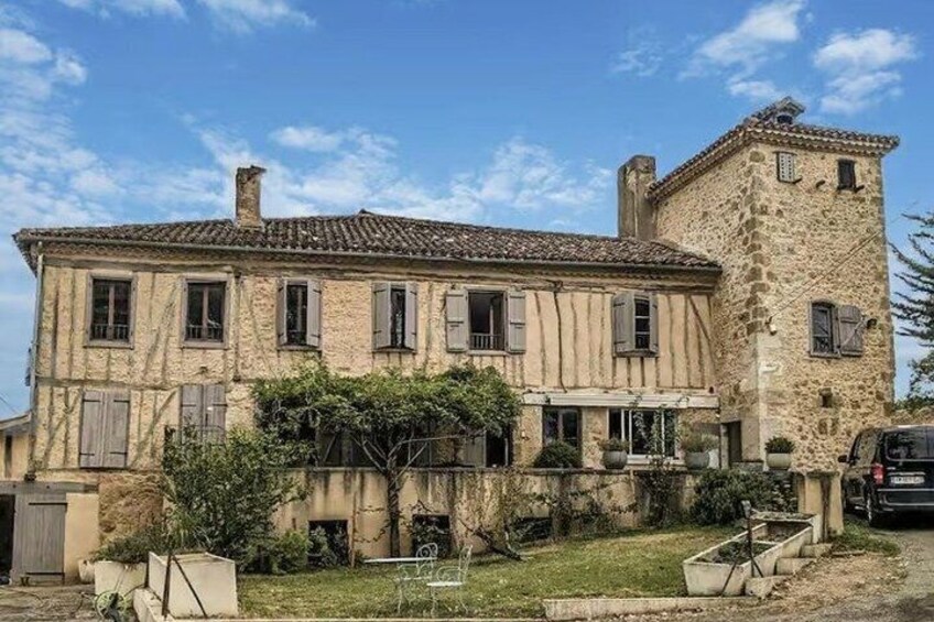 A stone building with a tower, a garden, and a parked car. 1