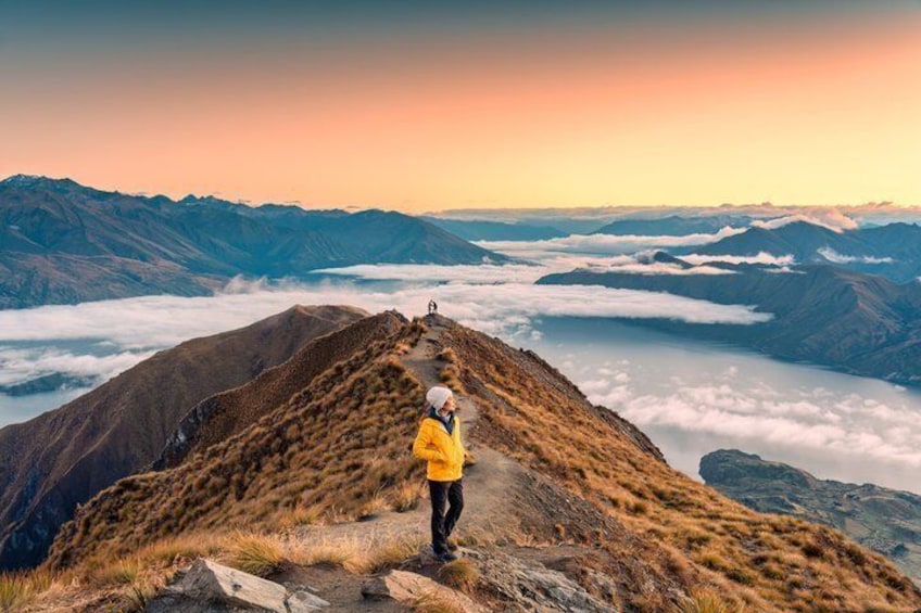A hiker in a yellow jacket on a mountain ridge with a view of a valley below. 1