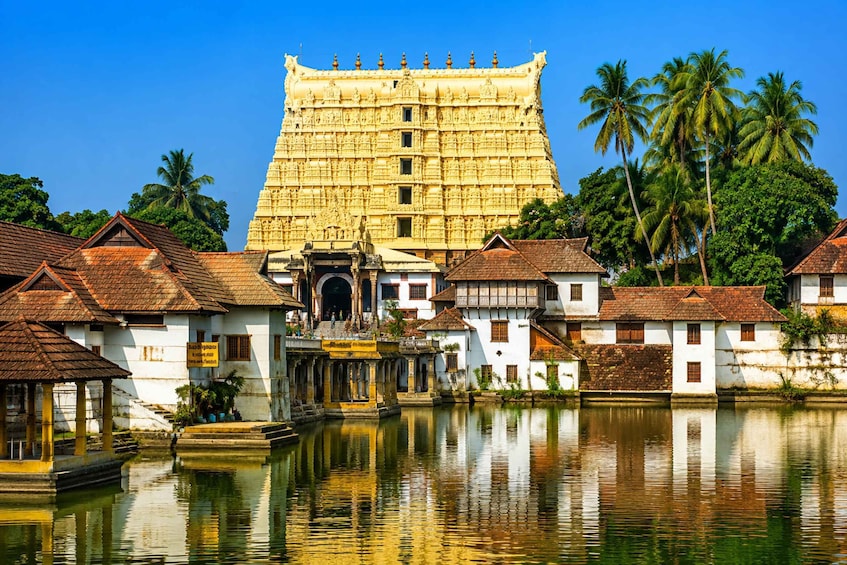 A traditional temple with intricate carvings, surrounded by white buildings with red roofs, palm trees, and a calm water body reflecting the structures. 5