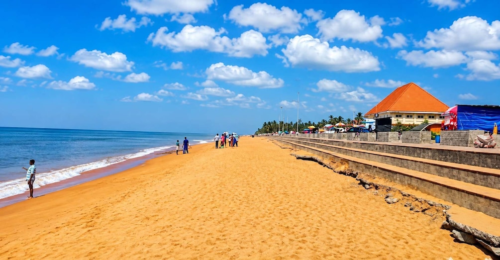 A sandy beach with a clear blue sky, a few people walking, and a building with a red roof in the background. 4