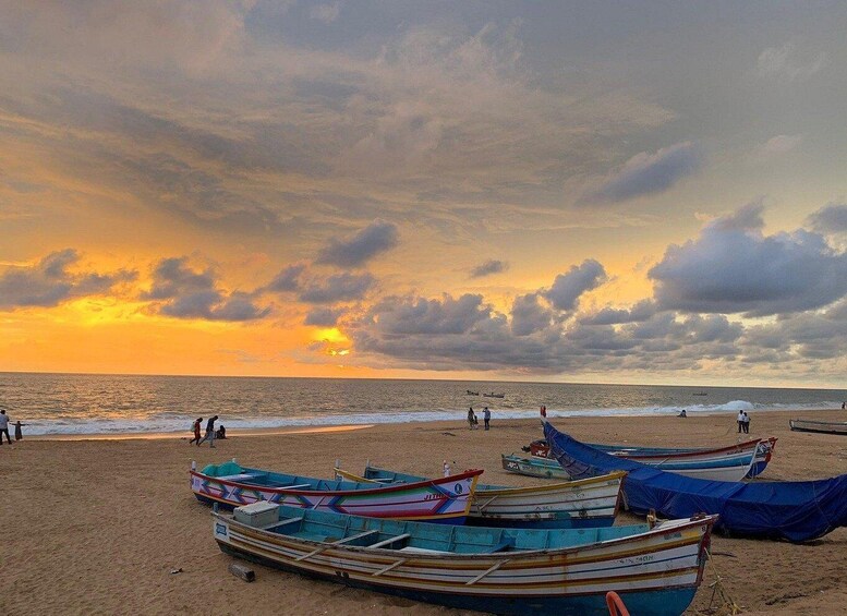 A beach at sunset with several colorful boats and people walking along the shore. 1