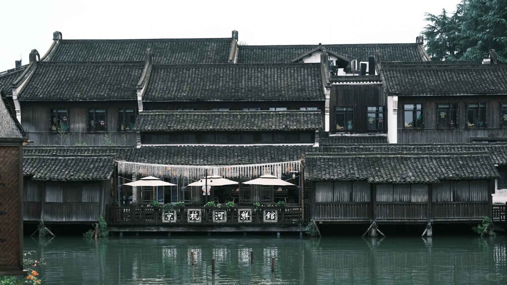 A traditional wooden building with a thatched roof, a waterway in front, and a sign with Chinese characters. 2