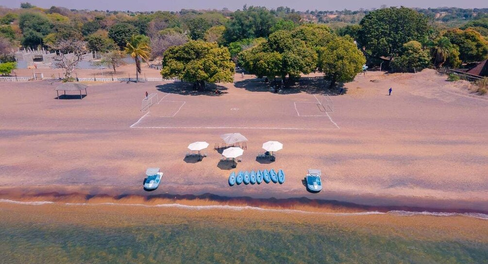 An aerial view of a beach with umbrellas, lounge chairs, and a row of boats. 1