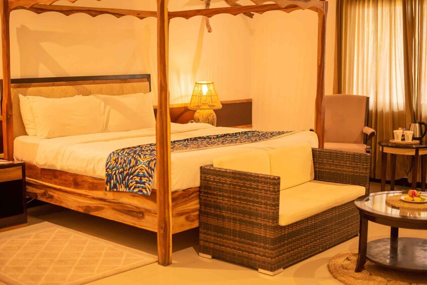A four-poster bed with a canopy, a bedside table with a lamp, a wicker armchair, a small round table with a teapot, and a decorative plate. 4