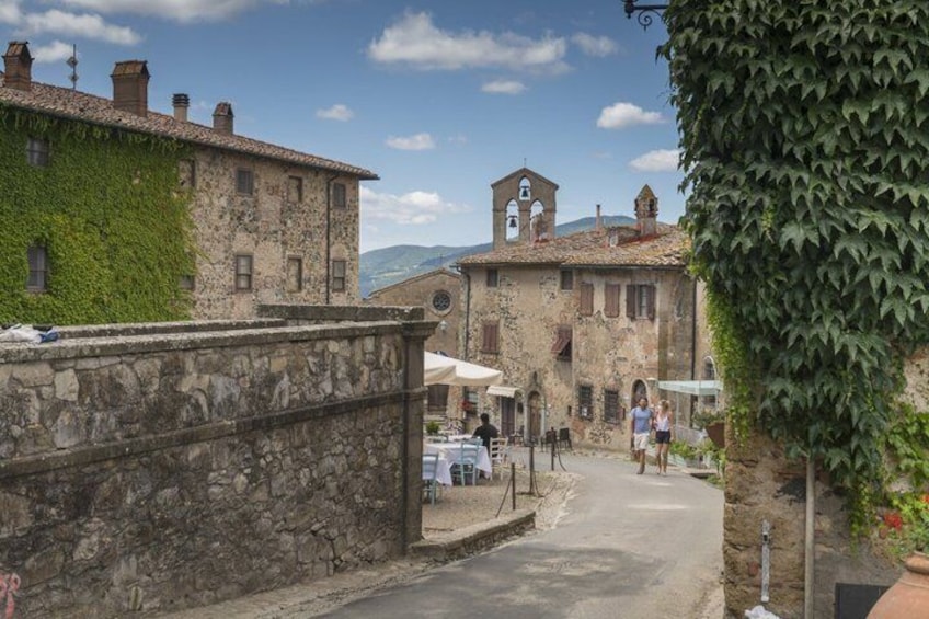 A narrow street in a historic town with stone buildings, a clock tower, and outdoor seating. 3