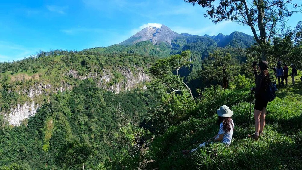 A mountainous landscape with a prominent volcano in the background, lush green vegetation, and a group of people hiking. 1