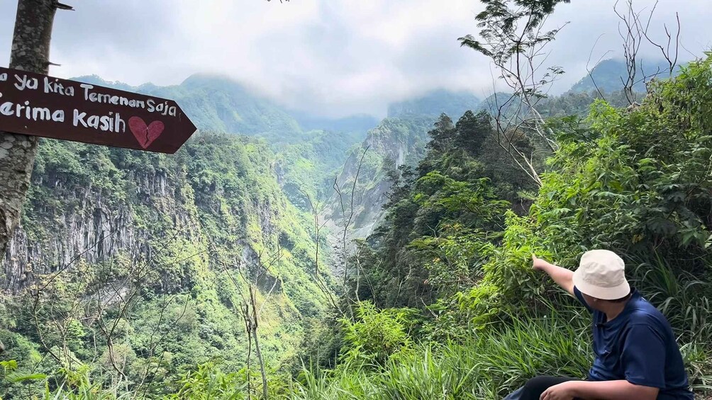 A person pointing at a sign with text in a mountainous landscape. 5