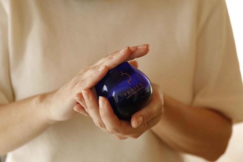 A person holding a dark blue bottle with gold lettering and a label that reads 'PERICA extra virgin olive oil.' 2