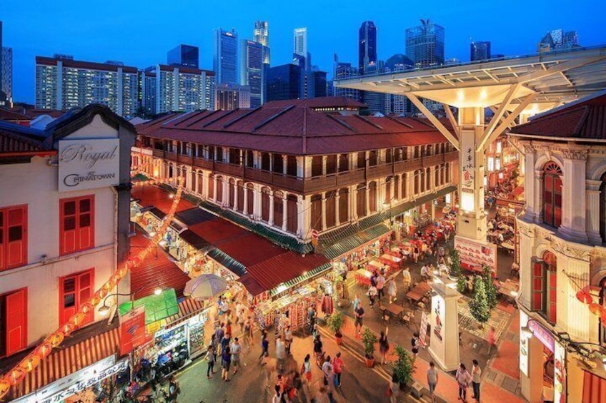 A bustling street market with traditional buildings and a city skyline in the background. 5