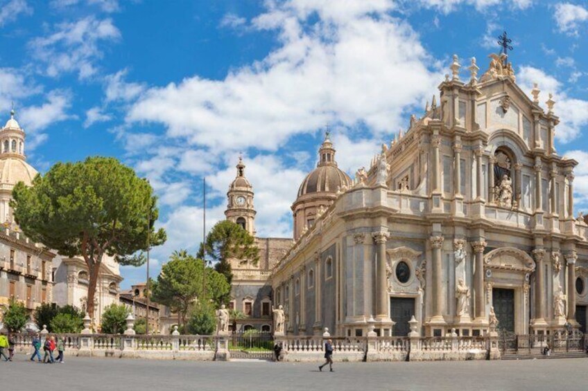 A grand historical building with domes and ornate architecture, surrounded by a spacious plaza with trees and a fence. 3