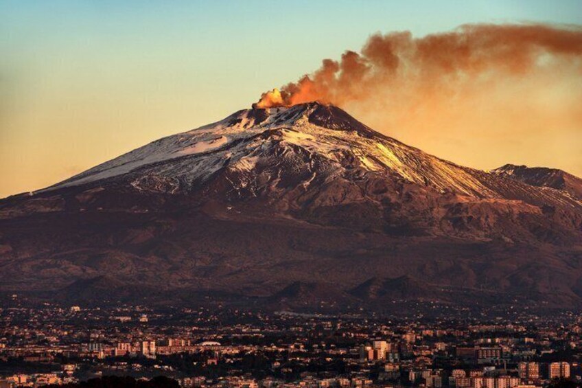 A snow-capped mountain with a plume of smoke, a cityscape below, and a clear sky. 4