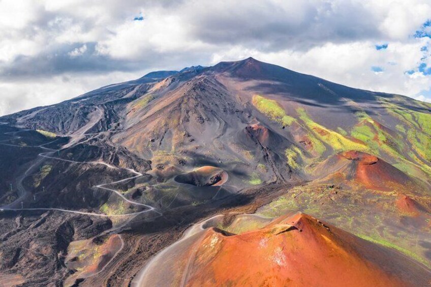 A volcanic landscape with distinct red and green areas, a crater, and a mountain range in the background. 2