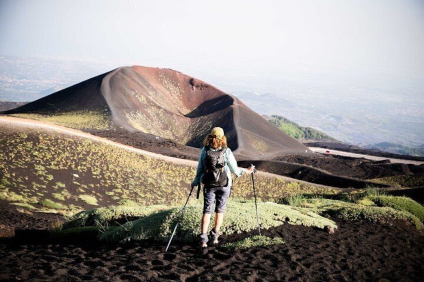 A person hiking on a volcanic landscape with a prominent lava flow in the background. 1