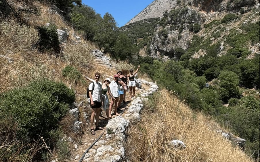 A group of hikers on a rocky trail surrounded by dry grass and trees. 4