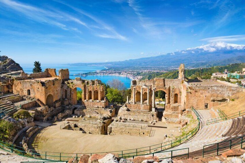 Ancient ruins with a large amphitheater, a sea view, and a distant mountain range. 4
