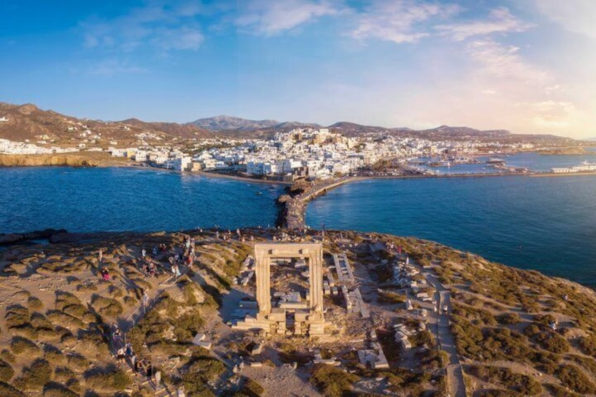 A coastal town with a prominent ancient structure, a harbor, and a mountainous backdrop. 1