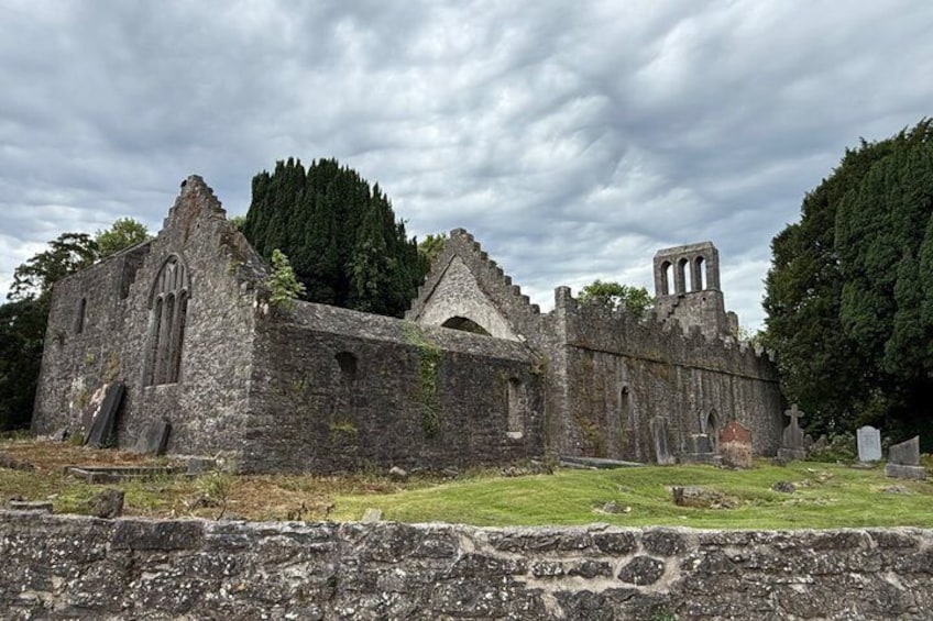 An old stone church with ruins, surrounded by grass and trees. 2