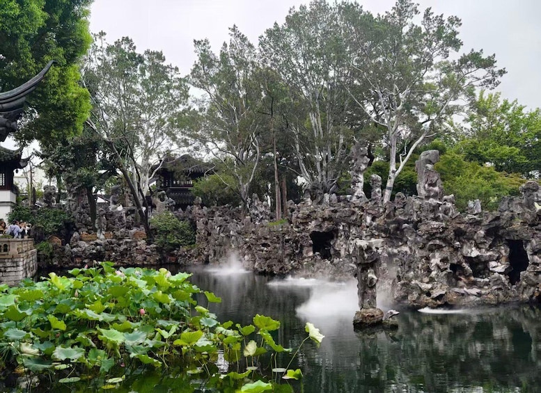 En traditionel kinesisk have med en bro af sten over et bassin, frodig vegetation og en pagode i baggrunden. 1