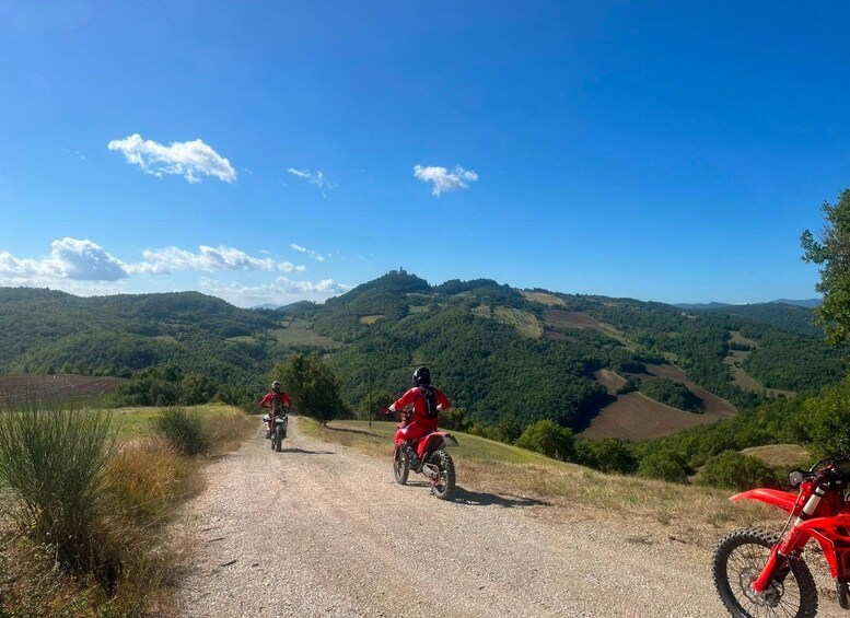 Two motorcyclists on a gravel path with a scenic view of rolling hills and a castle in the distance. 1