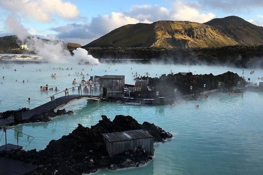 A geothermal spa with hot springs, a wooden bridge, and a mountainous backdrop. 2