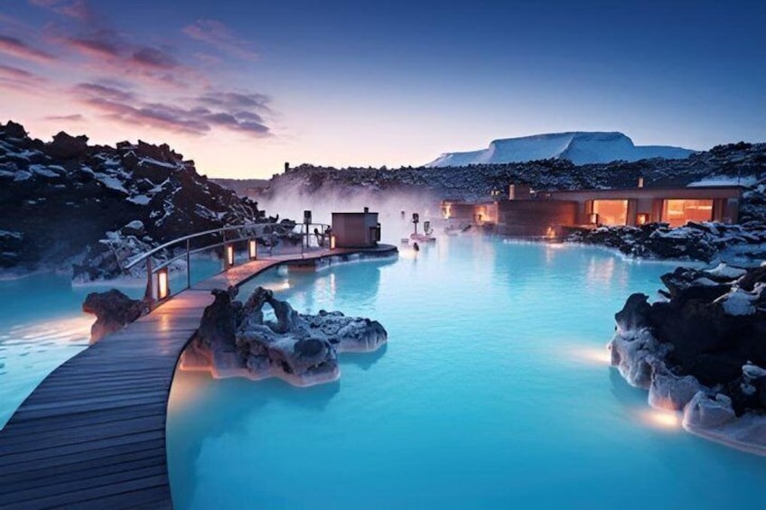 A geothermal spa with a wooden deck, a pool, and buildings with warm lights. 3