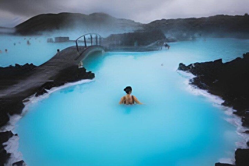 A person in a geothermal pool surrounded by volcanic rocks. 1
