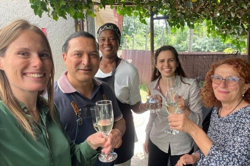 A group of people holding wine glasses, standing under a covered area with greenery in the background. 1