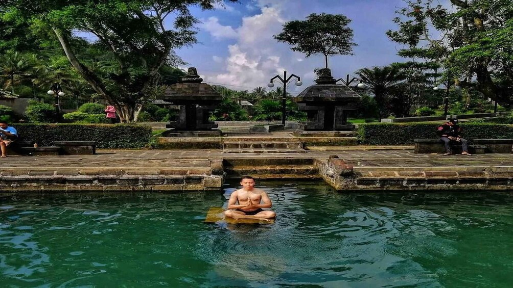 A person meditating in a pool surrounded by stone structures and greenery. 1