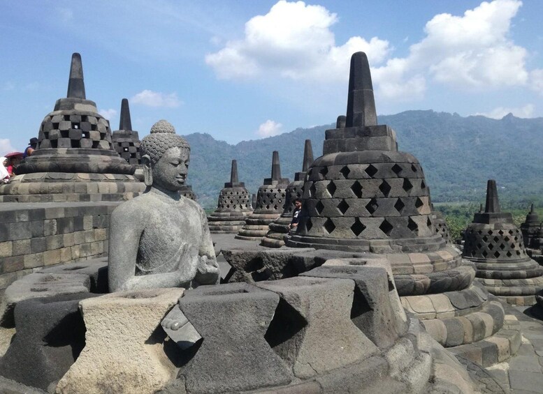 A large stone Buddha statue surrounded by smaller pagodas with mountains in the background. 4