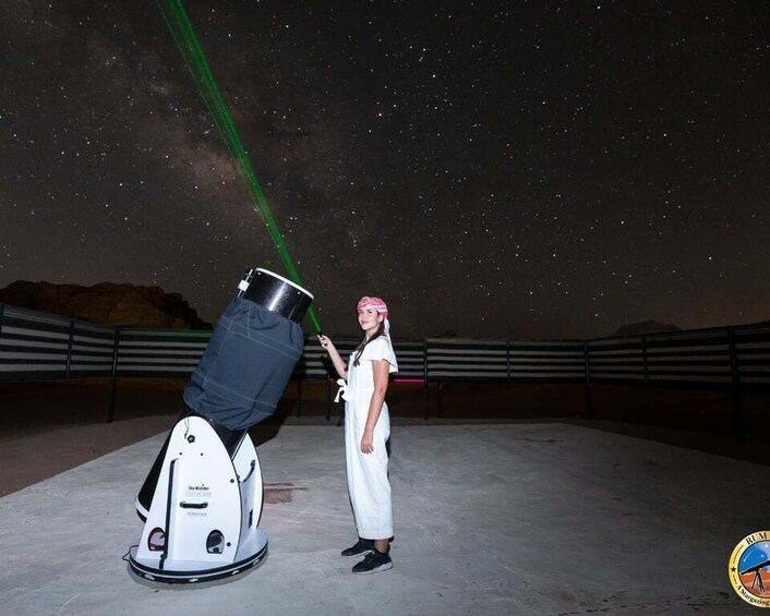A person standing next to a telescope with a green beam of light. 1