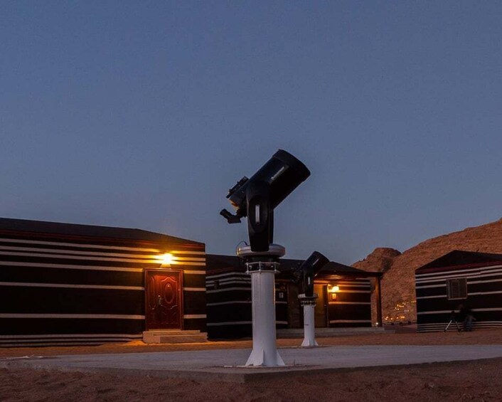 A telescope on a pedestal, a building with horizontal stripes, and a desert landscape at dusk. 5