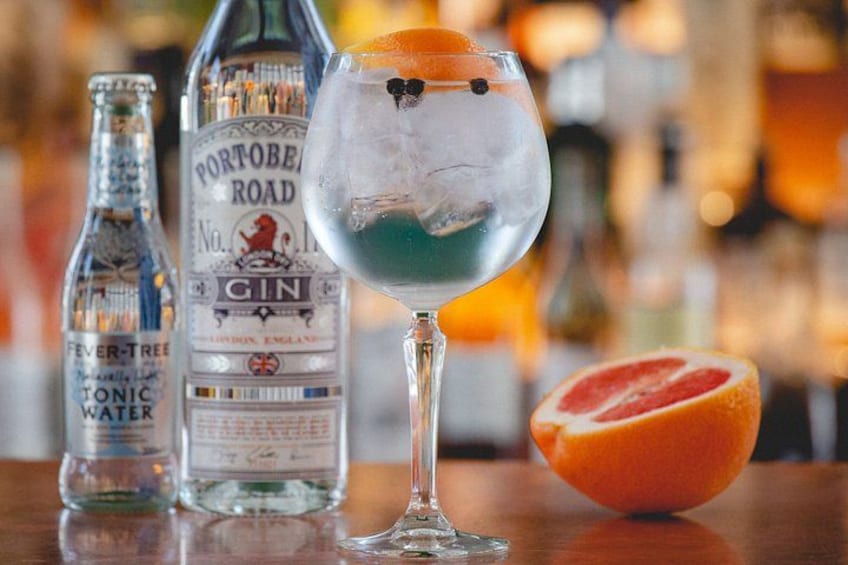 A cocktail glass with ice and a slice of orange, a bottle of Portobello Road Gin, and a bottle of Fever Tree Tonic Water. 3