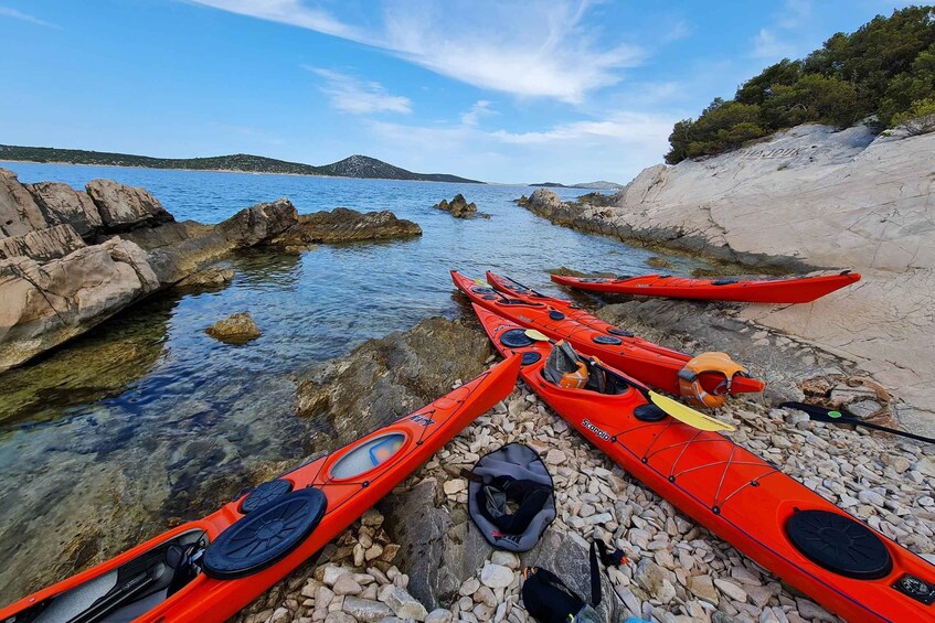 A row of red kayaks on a rocky shore with clear water and a distant island. 3