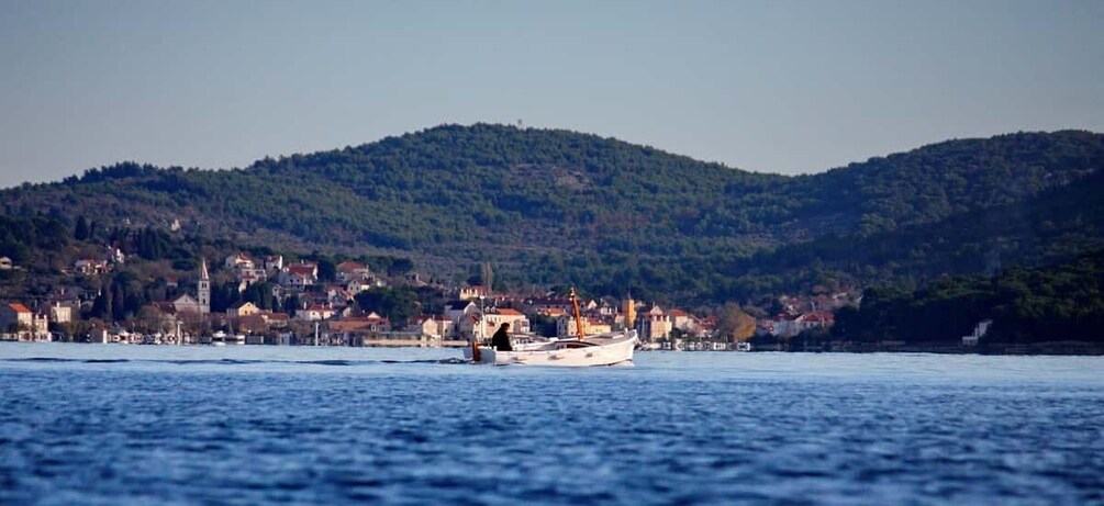 A boat on a calm body of water with a town and hills in the background. 1