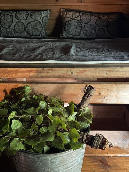 A rustic wooden bench with patterned cushions, a metal bucket with green foliage, and a wooden plank. 2
