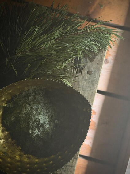 A wooden surface with a decorative metal bowl and green pine branches. 5