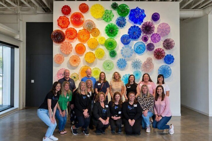 A group of people posing in front of a colorful glass art installation. 5
