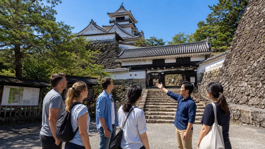 A group of tourists at a historical site with traditional architecture, including a multi-tiered building and stone steps leading to a gate. 1
