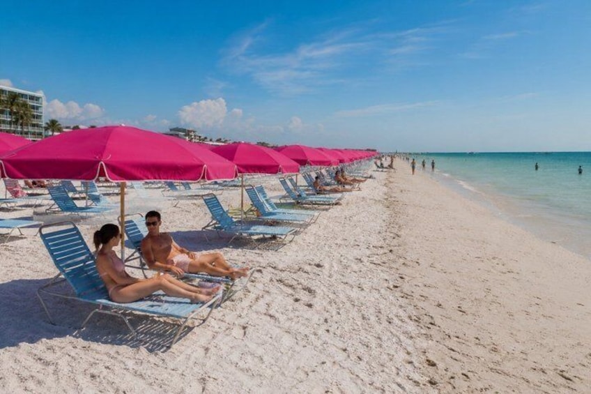 A beach with rows of blue lounge chairs and pink umbrellas. 4