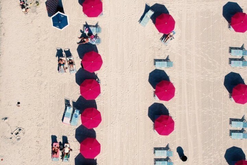 An aerial view of a beach with rows of umbrellas and lounge chairs. 2