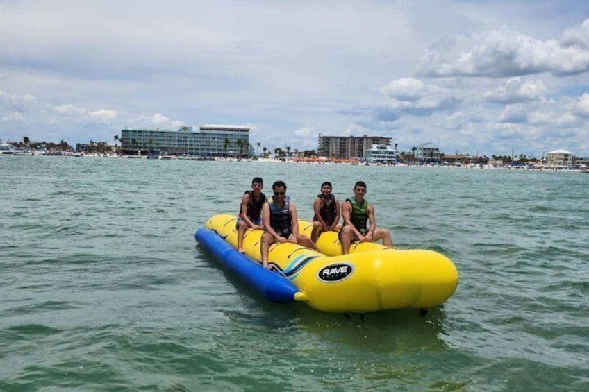 A yellow inflatable raft with three people on a body of water, with buildings and a beach in the background. 5