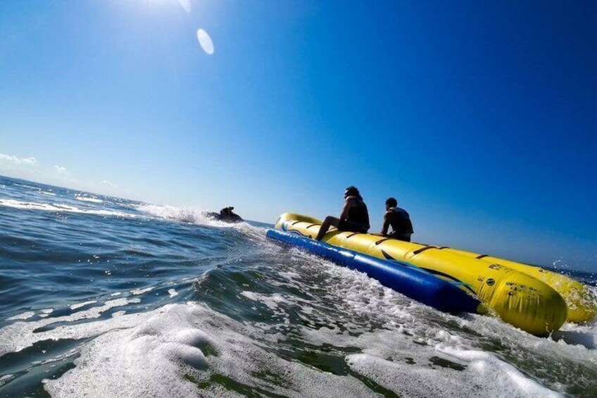 A person riding a yellow inflatable raft on the ocean, another person sitting on the raft, and a third person in the water. 2