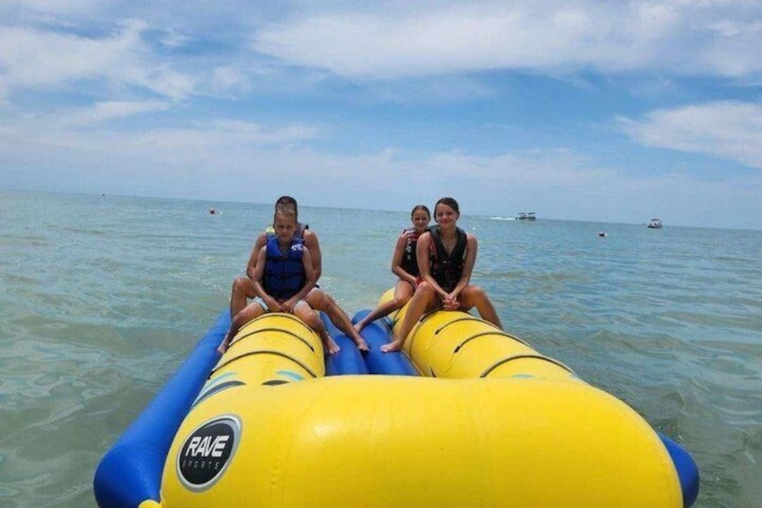 Three people on a yellow and blue inflatable raft in the ocean with boats in the background. 4