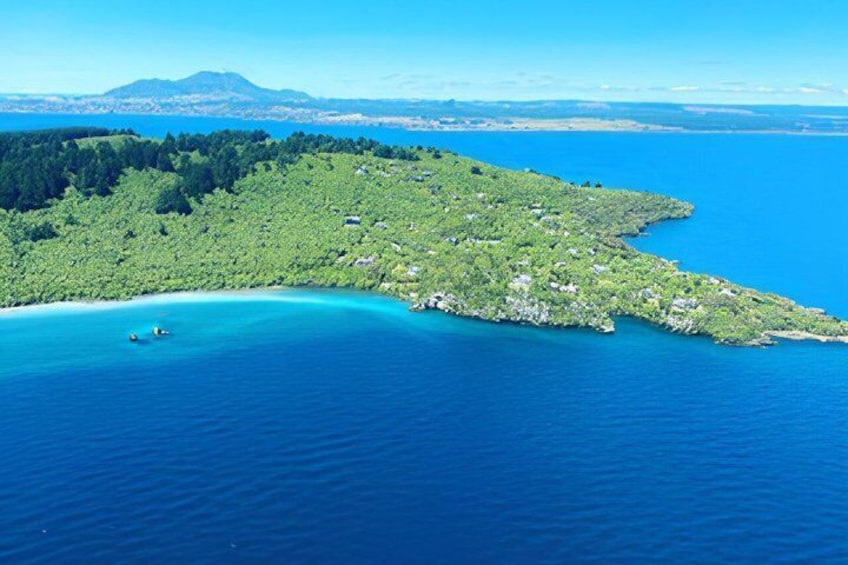A coastal landscape with a clear blue sea, a green forested island, and a distant mountain range. 2