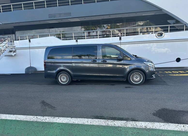 A dark-colored minivan parked in front of a large white boat with a green area in the foreground. 5