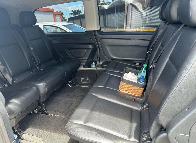 A car's interior with black leather seats, a center console, and a rear storage compartment containing a bottle and a box. 2