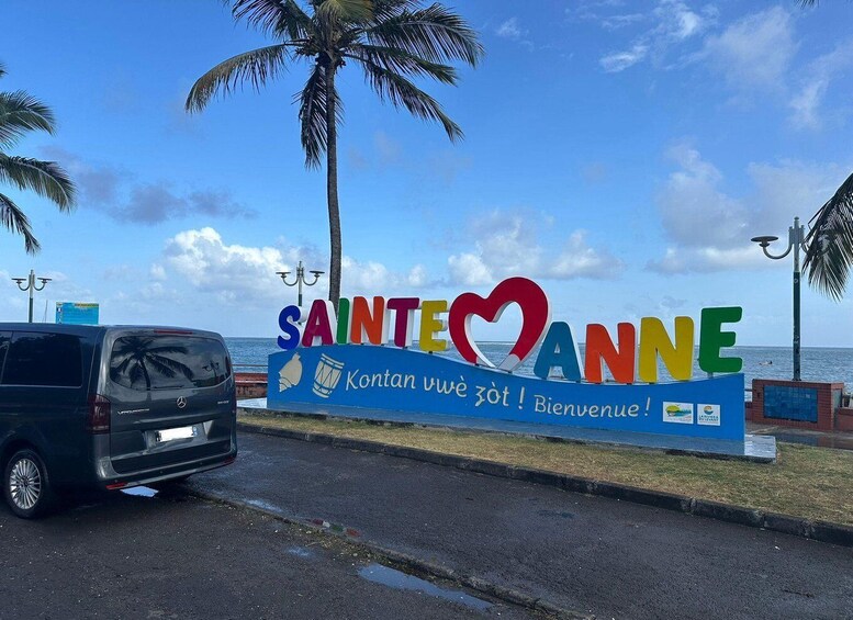 A sign with 'SAINT-ANNE' and a heart symbol, a Mercedes van, palm trees, and a beach in the background. 3