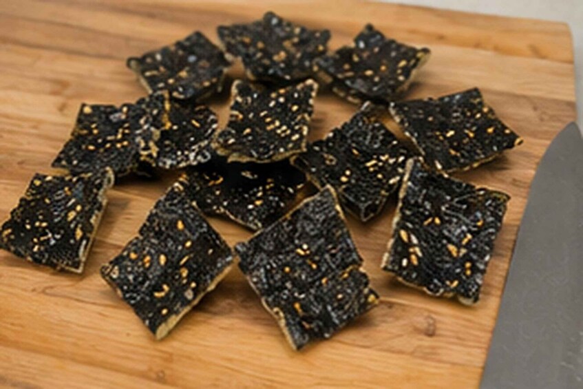 A wooden cutting board with several pieces of dark-colored, textured food items with visible seeds. 2