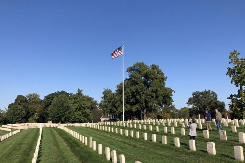 A cemetery with rows of headstones, an American flag, and trees in the background. 3